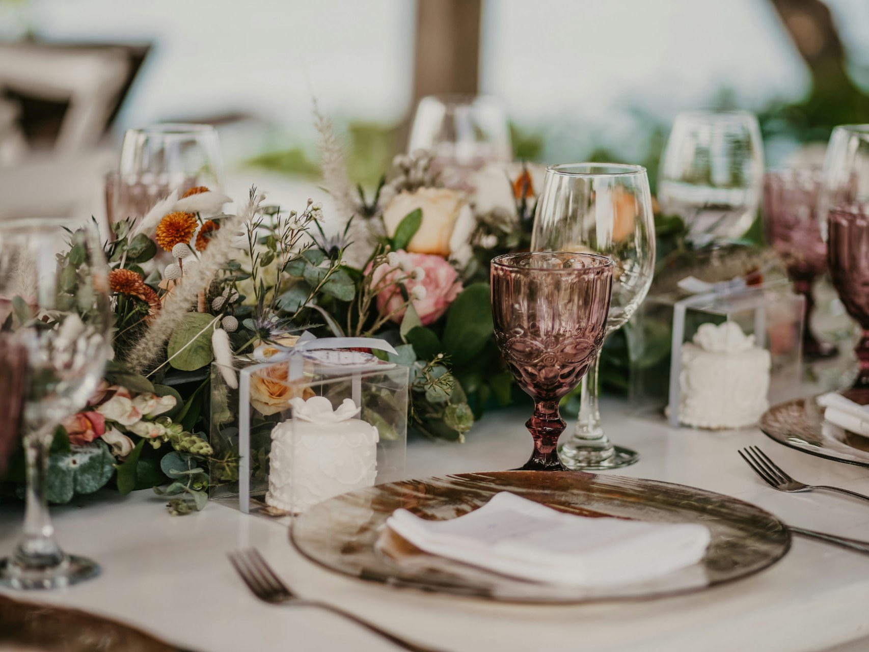 Festlich gedeckte Gästetafel mit Blumenläufer aus Rosen und Eukalyptus, rosafarbenen Weingläsern, Tortenboxen mit weissen Törtchen und Tellern mit weissen Servietten
