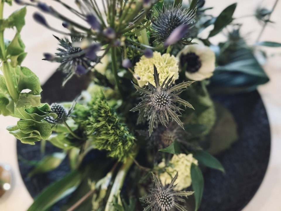 Blumenarrangement aus Disteln, Glocken- und Zwiebelblüten auf dunkler Unterlage, von oben gesehen