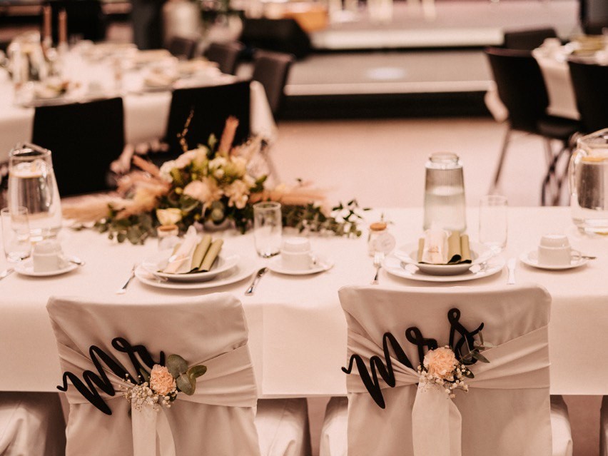 Festlich gedeckter Brauttisch mit «Mr & Mrs»-Schild, Kerzen und einem Blumengesteck in der Tischmitte