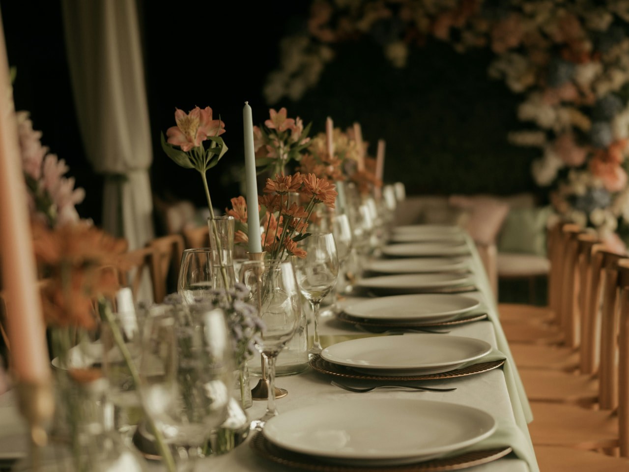 Lange Festtafel im Zelt mit weiss eingedeckten Tellern, Orangeblüten, mintgrüner Kerze und Lichterketten über dem Tisch