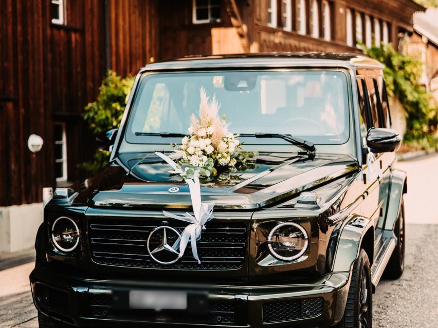 Blumenschmuck aus Rosen und Efeu auf der Motorhaube eines weissen Hochzeitsautos