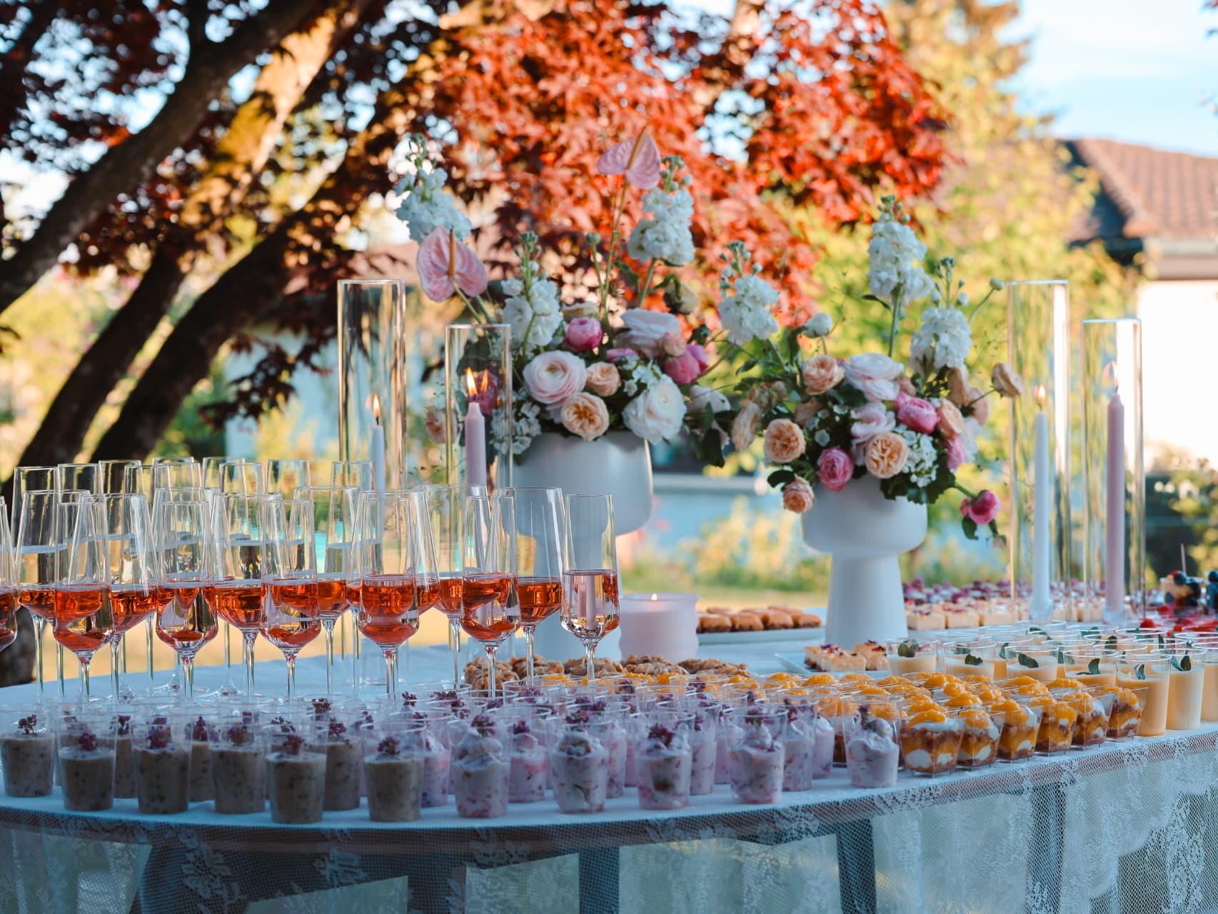 Dessertbuffet im Freien mit weissen Blumenvasen, Kerzen in Glaszylindern, Roséweingläsern und Häppchen