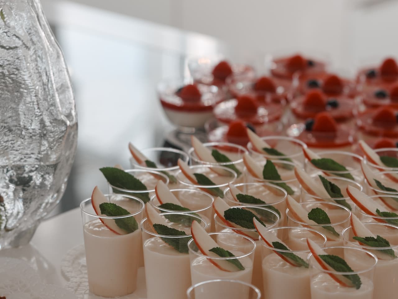 Vase mit orangen Blumen und hellen Schleierblüten neben Dessertgläsern mit Apfelscheibe und Minze