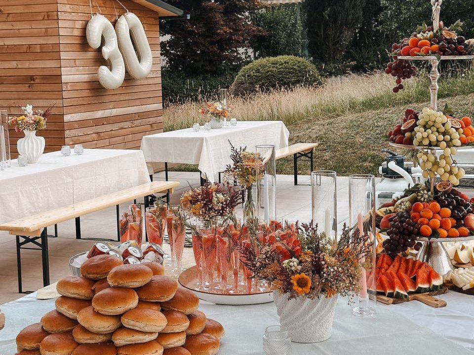 Apéro- und Dessertbuffet im Garten zum Geburtstag mit Brothaufen, Früchte-Etagere, roséfarbenen Gläsern und Herbstblumen vor dem Holzhütten-Schriftzug 30