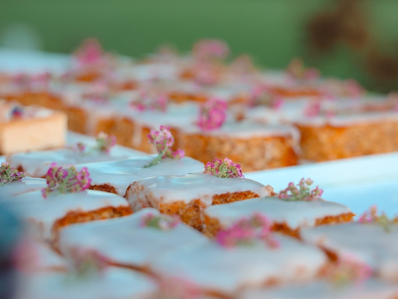 Kuchenstücke mit weisser Glasur und rosa essbaren Blüten auf einer Tafel im Freien