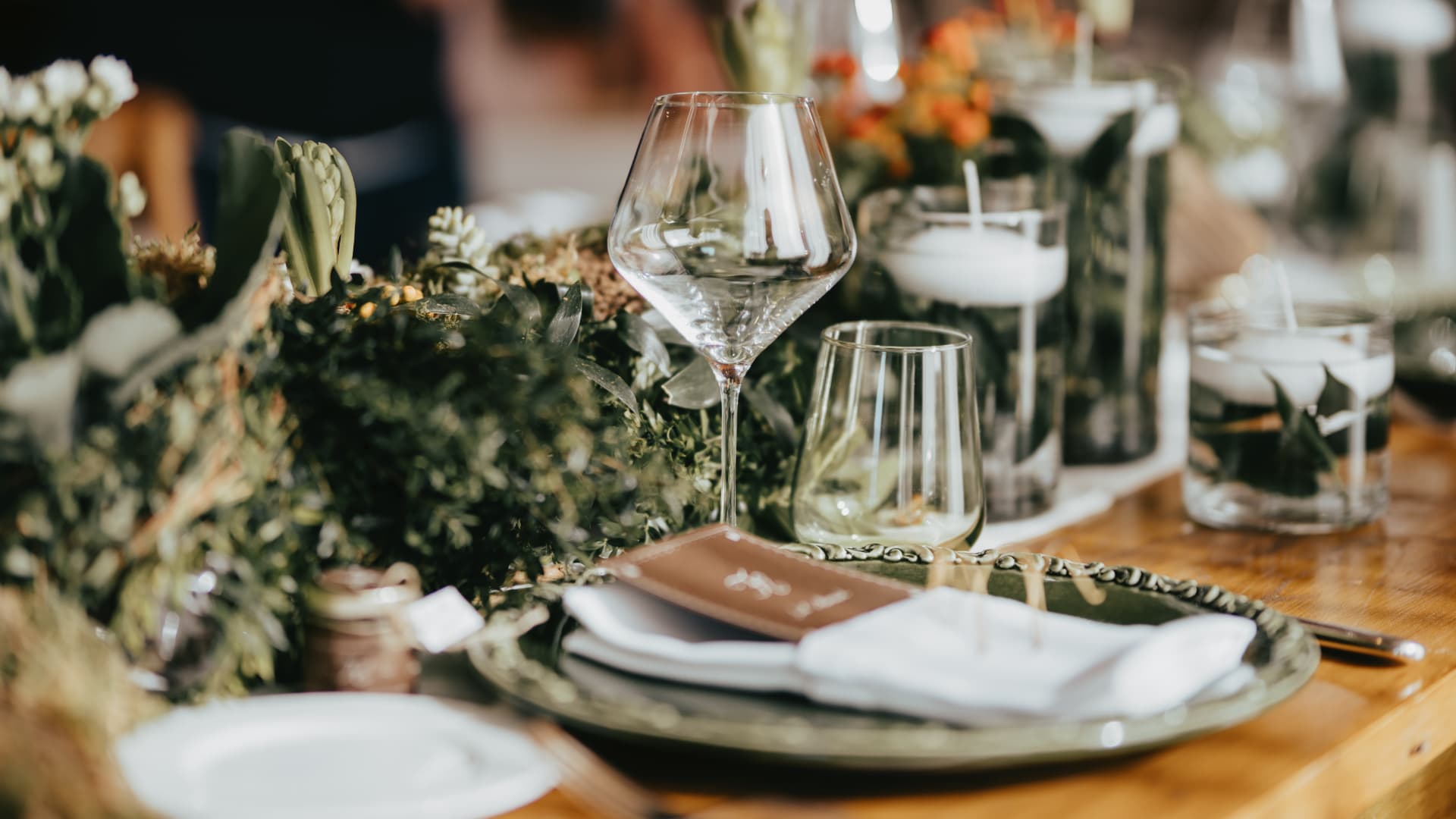 Gedeckter Tisch mit dunkelgrüner Keramikplatte, weisser Serviette, Menükarte und botanischem Läufer aus Moos, Grün, weissen Knospen und orangefarbenen Blüten